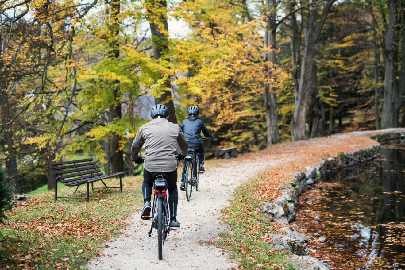 To mennesker cykler igennem en efter&aring;rsskov med cykelhjelm p&aring;.