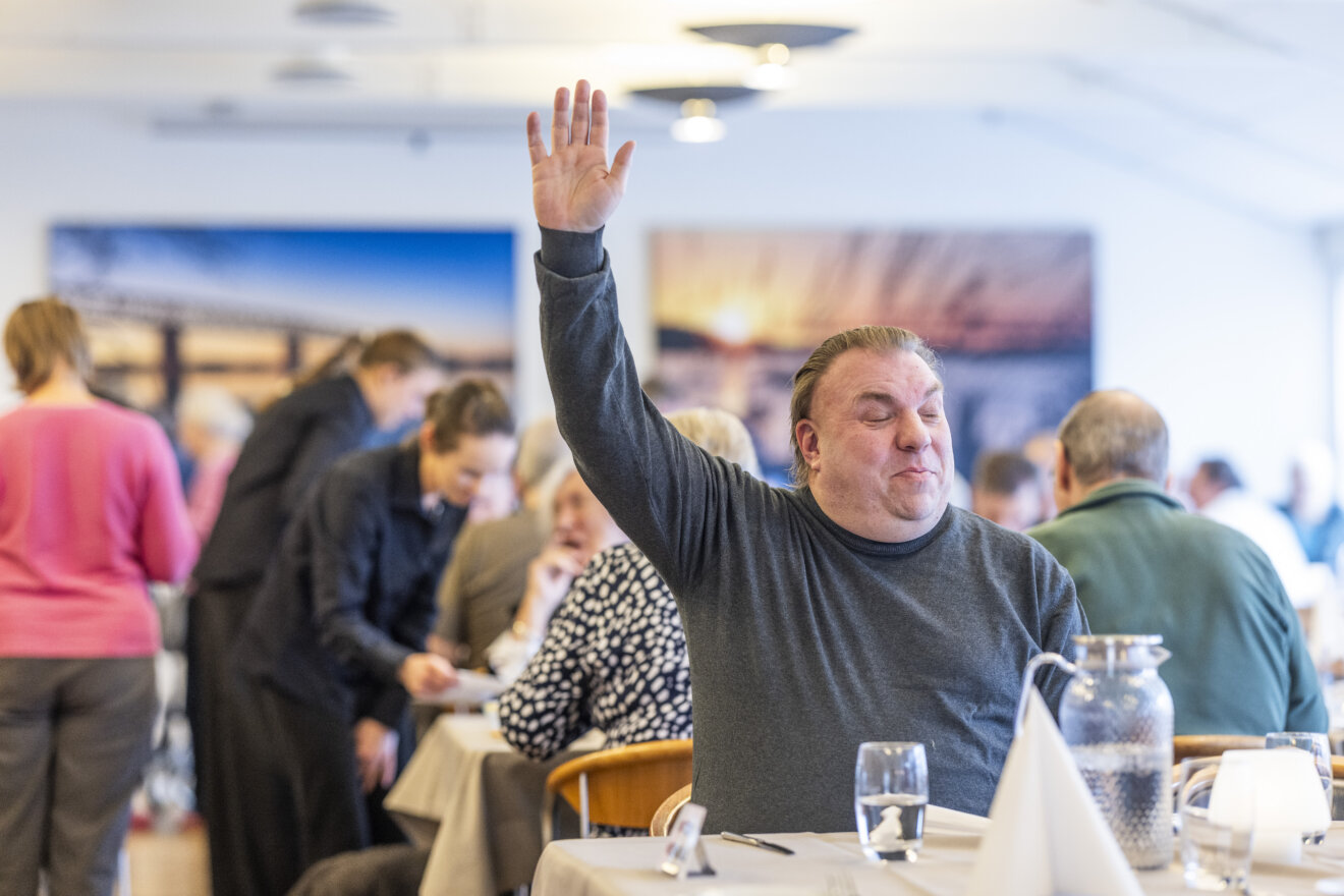 En mand sidder i restauranten. Han har rakt en arm i vejret.