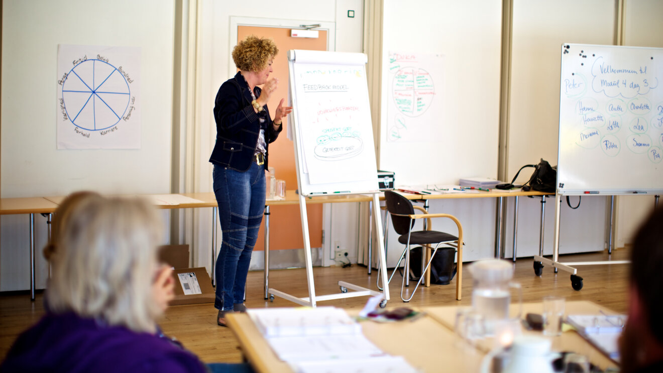 En kvinde står ved en flip-over og facilitere gruppearbejde.